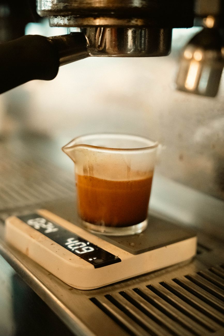 Detailed view of espresso brewing into a glass cup placed on a digital scale under a coffee machine.