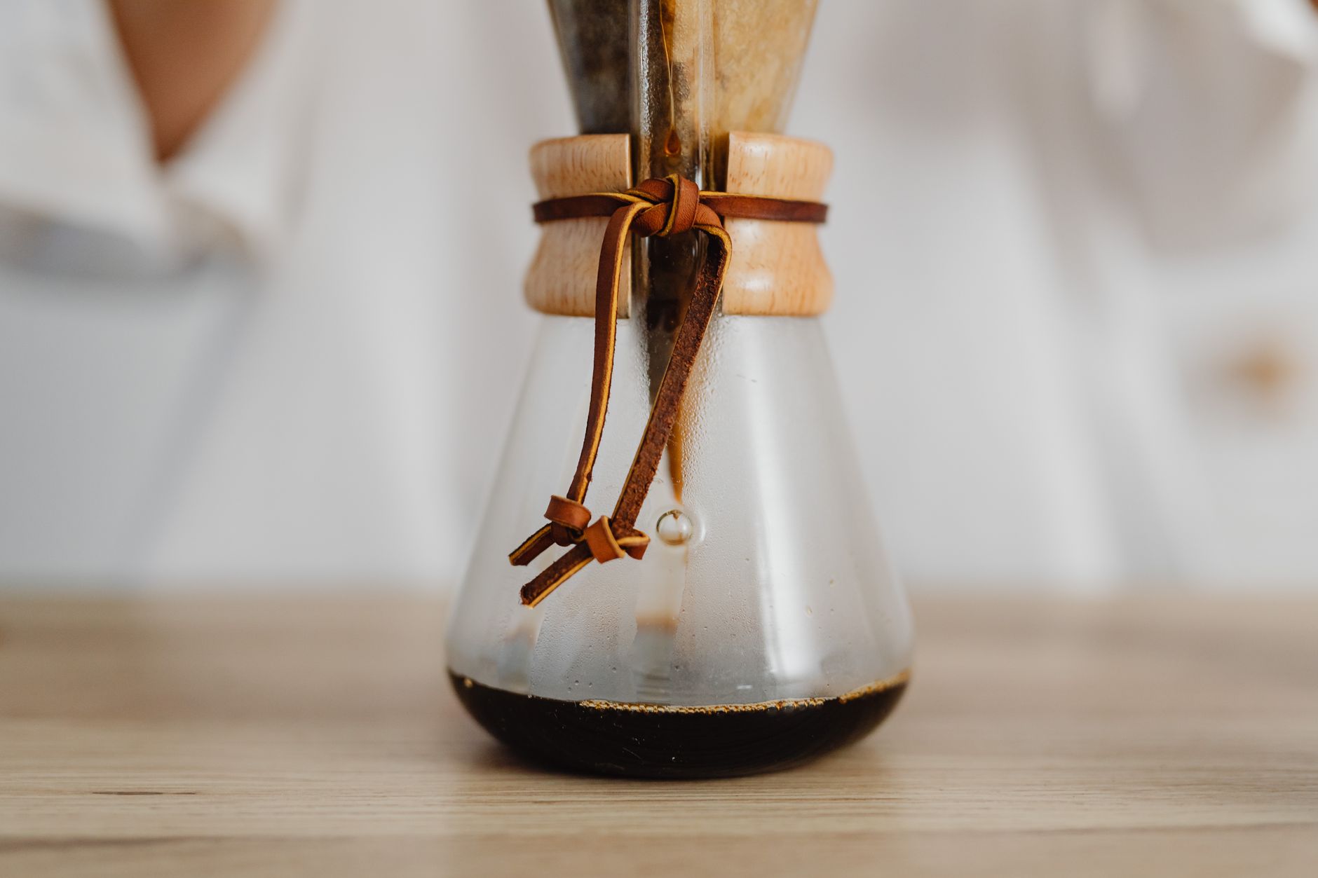 A detailed view of a Chemex coffee maker with freshly brewed drip coffee on a wooden surface.