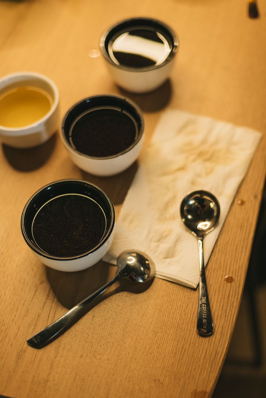 A warm coffee tasting setup with cups and spoons on a wooden table.