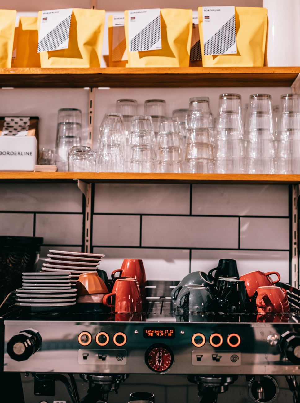 Professional coffee maker with cups and saucers under transparent glasses and row of packages in cafeteria kitchen